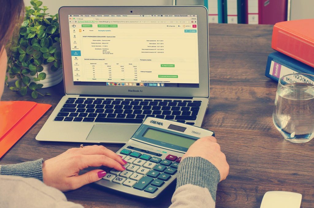 Mains sur une calculatrice devant un ordinateur portable, calcul d'un budget netlinking