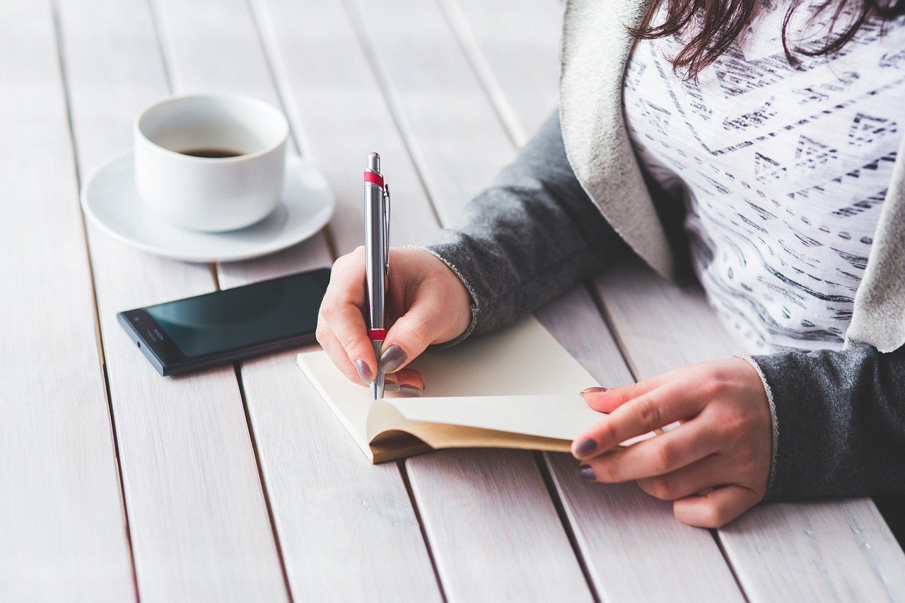 Personne notant une liste de questions dans un carnet à côté d'un café