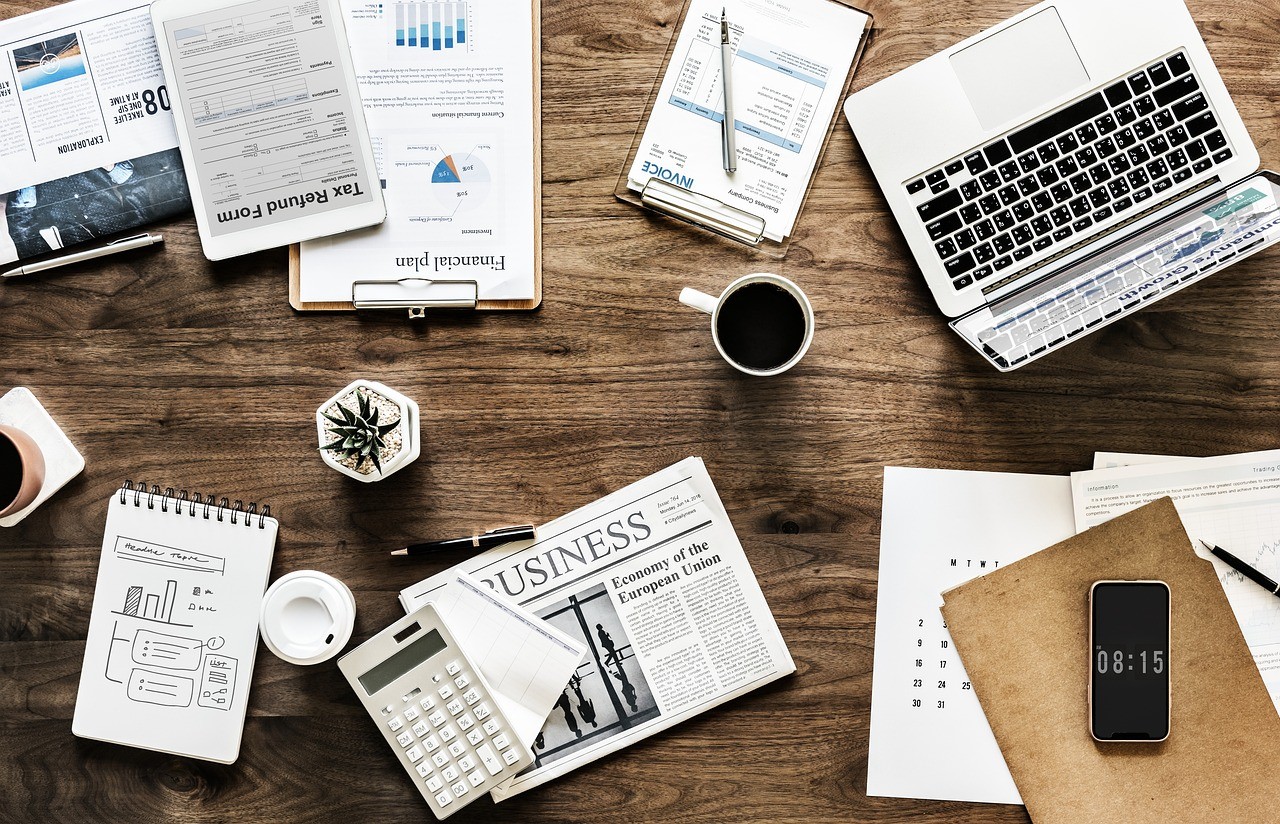 Bureau de travail avec ordinateur portable, documents, journal et café pour planifier ses contenus
