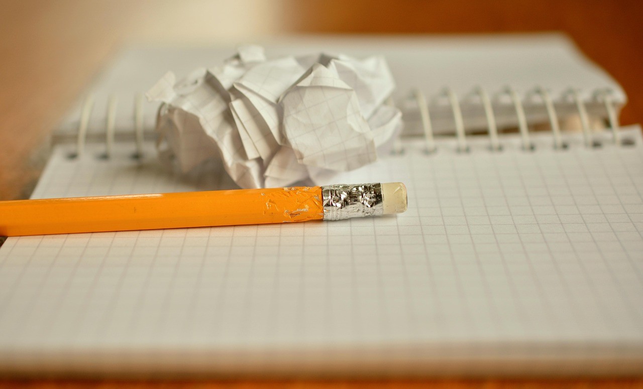Une boule de papier froissé posée sur un carnet à spirale avec un crayon