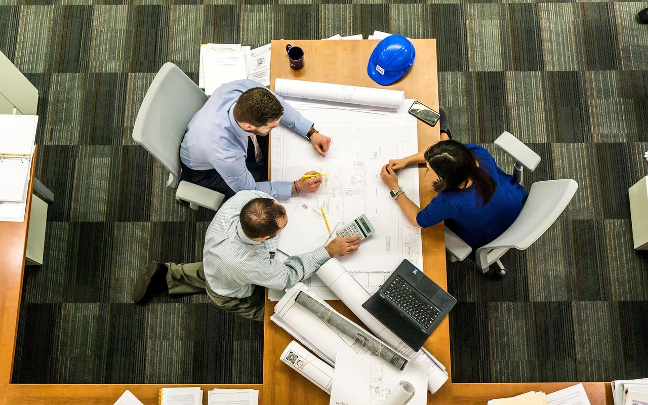 Vue de dessus d'une équipe réunie autour d'une table de travail couverte de plans et de documents