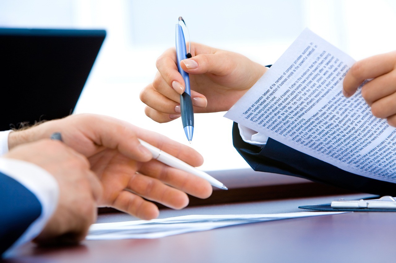 Deux personnes échangent et annotent un document de travail autour d'un bureau