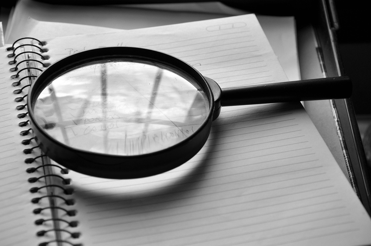 Une loupe posée sur un carnet ouvert, évoquant une vérification page par page