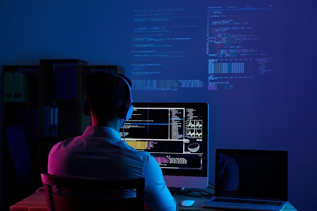 Développeur web au travail devant plusieurs écrans de code, la nuit