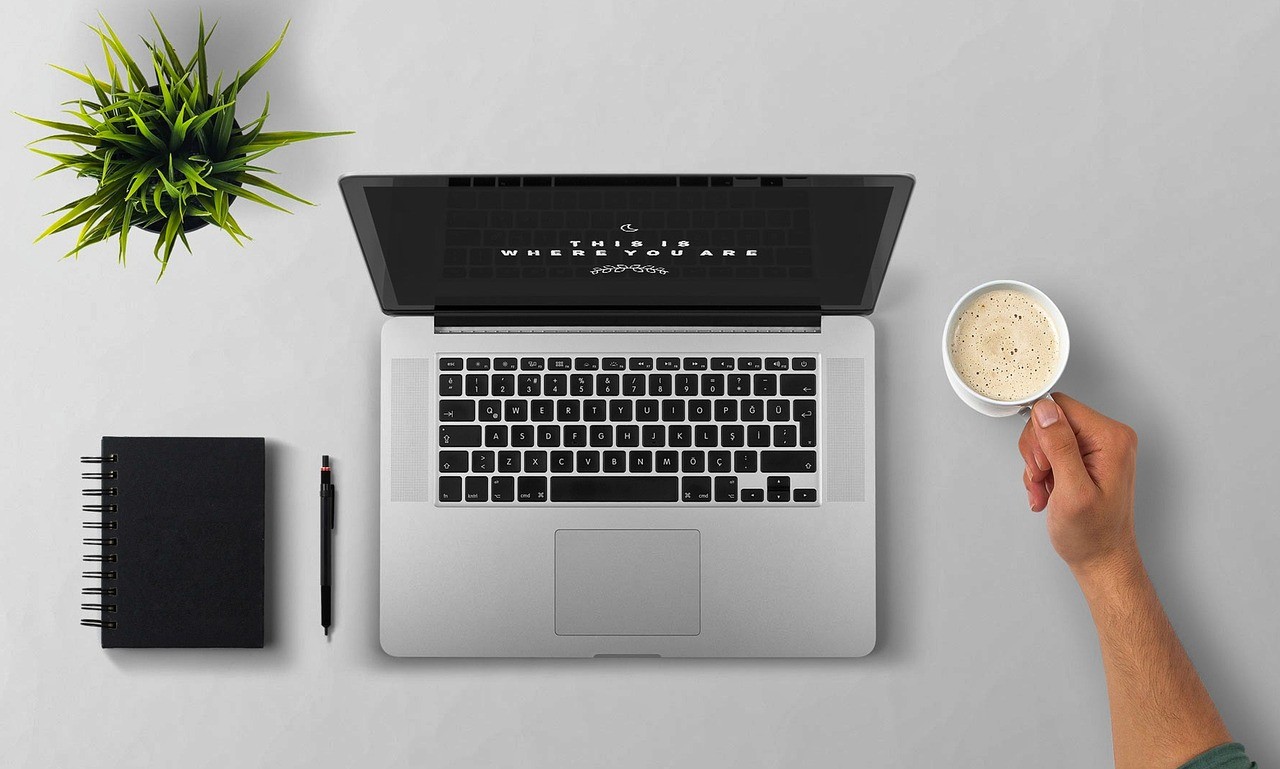 Poste de travail avec ordinateur portable, café et carnet, vu de dessus, évoquant le suivi quotidien d'un site par son gestionnaire