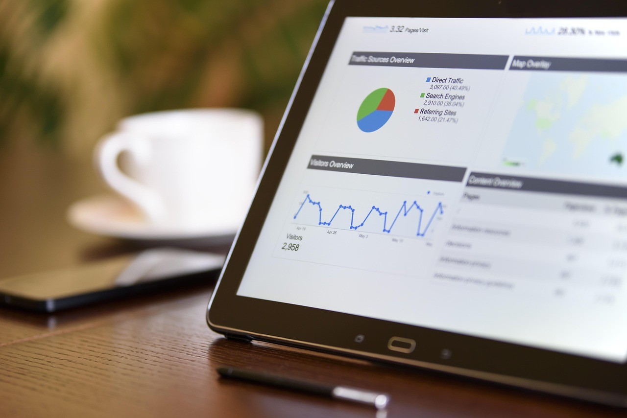 Une tablette affiche un rapport de trafic et de sources d'audience sur un bureau en bois, à côté d'une tasse de café