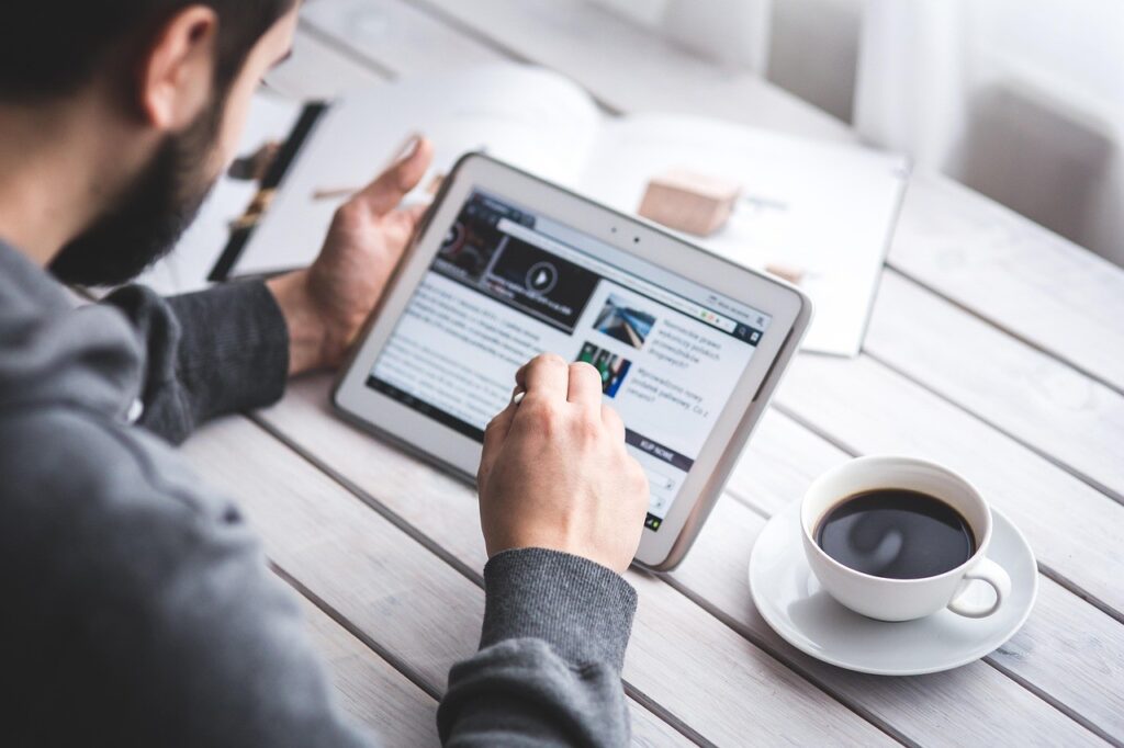 Une personne lit l'actualité sur une tablette numérique, tasse de café à côté