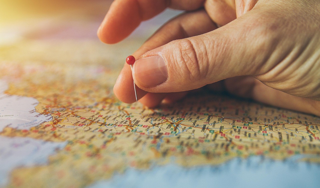 Une main plante une épingle sur une carte en papier, symbole du repérage local