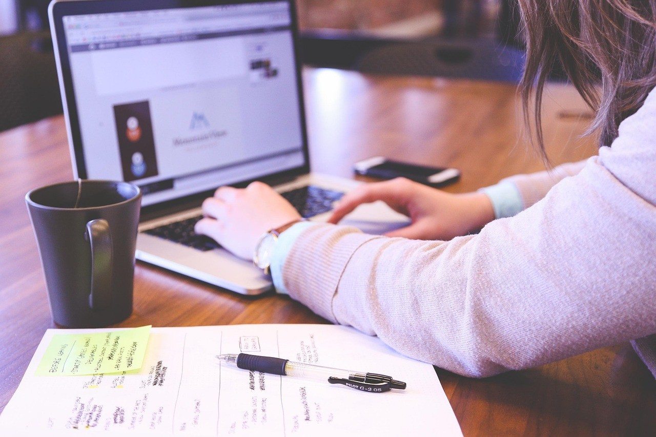 Une personne tape sur le clavier d'un ordinateur portable face à un site web affiché à l'écran