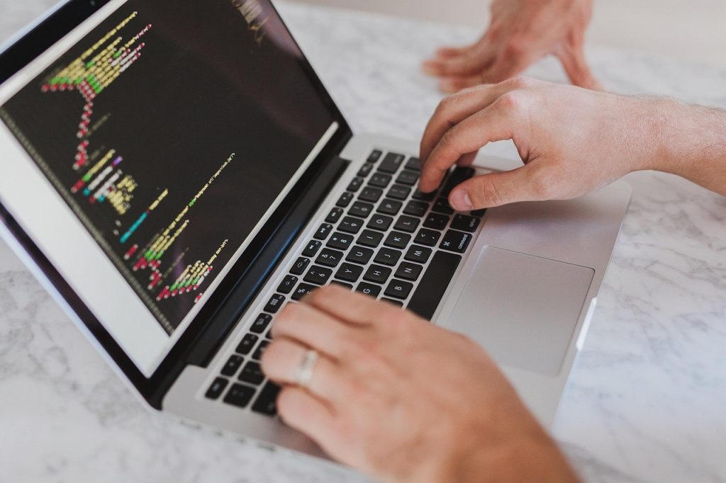 Mains tapant sur un clavier d'ordinateur portable face à un écran de code