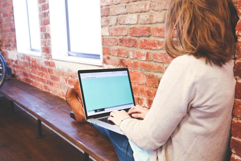 Une personne rédige du contenu sur son ordinateur portable dans un café lumineux