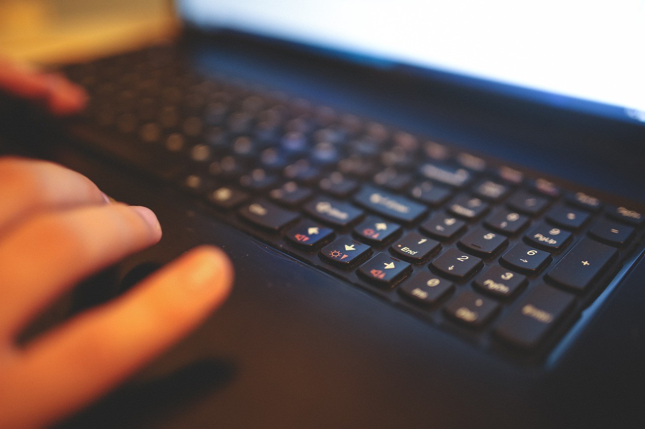 Mains sur le clavier d'un ordinateur portable, écran allumé en arrière-plan