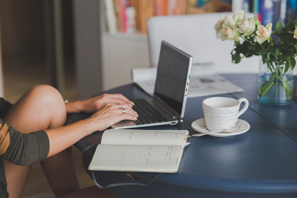 Personne qui rédige du contenu web sur un ordinateur portable, tasse de café à côté
